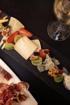 cheeseboard with fruit, cava, and iberian ham charcuterie on black table, contrast
