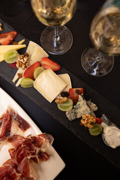 cheeseboard with fruit, cava, and iberian ham charcuterie on black table, contrast