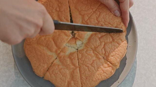 Soft orange sponge cake sliced on plate with serrated knife, closeup topdown view showing crumbly texture and tender interior, home baking scene with careful hand guiding knife, natural light