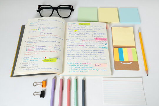 Top view of an open notebook with handwritten notes, colorful markers, sticky notes and glasses. Concept of studying, productivity, organization and creative learning.