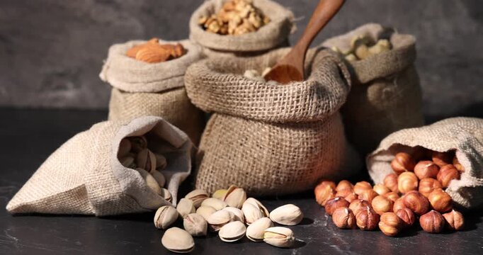 Different types of nuts in bags on black table, closeup. Camera moving right
