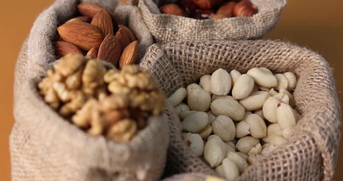 Different types of nuts in bags on brown background, spinning. Closeup view