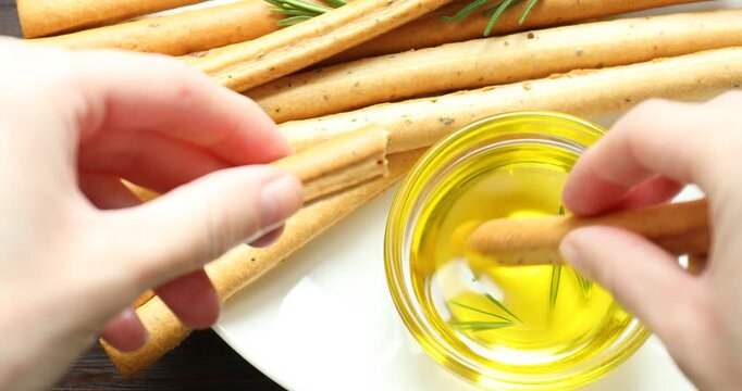 Woman breaking grissini breadstick and dipping into oil at wooden table, top view