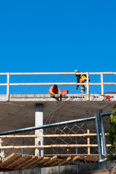 Construction worker high up on building project working on grouting structural post-tensioning wire strand holes running through concrete slab of floor
