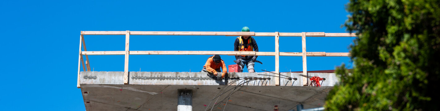 Construction worker high up on building project working on grouting structural post-tensioning wire strand holes running through concrete slab of floor
