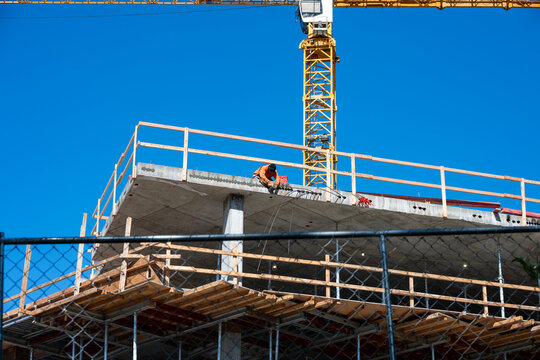 Construction worker high up on building project working on grouting structural post-tensioning wire strand holes running through concrete slab of floor
