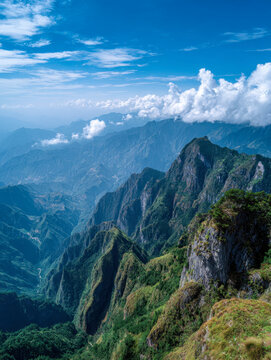 Breathtaking panoramic view of lush green mountain ridges and deep valleys under a vibrant blue sky with scattered white clouds in a pristine natural landscape