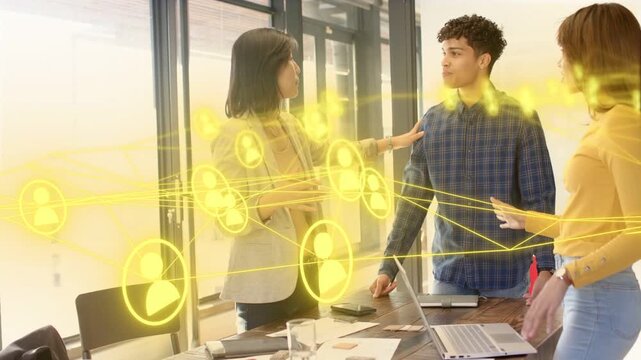Left woman gesturing, aligning team at table, animated yellow network flowing over laptop, business