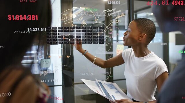 Female lead lifting marker, marking grid on glass and showing finance overlays for budget review