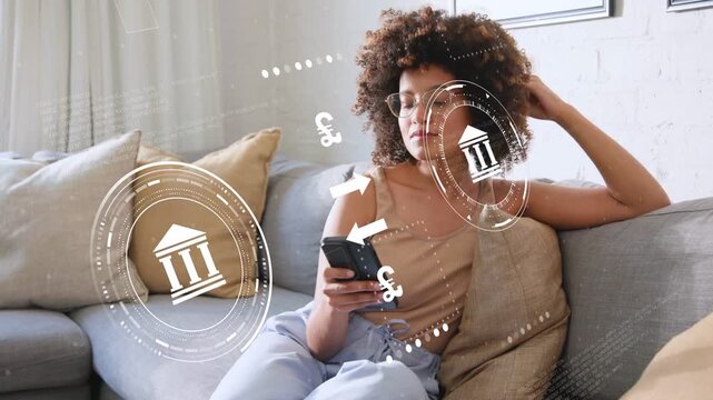 Woman shifting on sofa, tapping phone as banking HUD overlaying currency icons managing funds