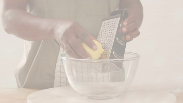 Home cook pressing lemon against box grater over glass bowl, producing fine shavings for recipe
