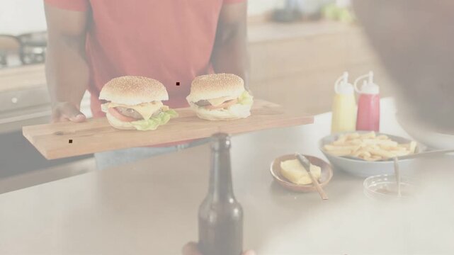 Adult son sliding board across kitchen island, presenting burgers and condiments for family meal