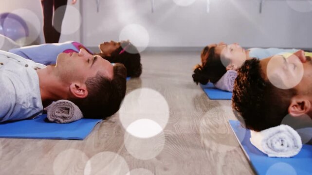 Instructor cueing breath while fitness group resting on blue mats, towels shifting, bokeh drifting