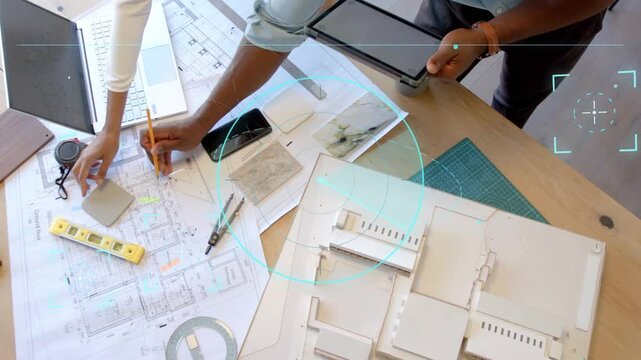 Two architects tapping tablet, placing sample and marking plan, reviewing design with circular UI