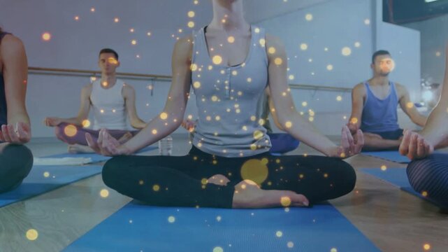 Camera lifting from blue mat showing woman closing eyes guiding group into yoga with gold particles