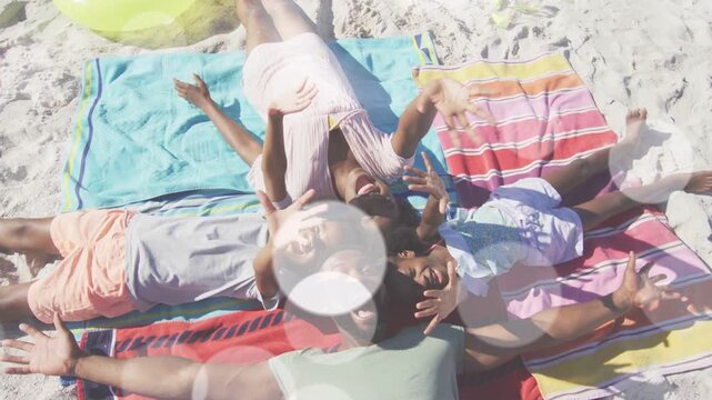 Family lying head-to-head on towels, drone hovering overhead, lifting arms, creating travel ad