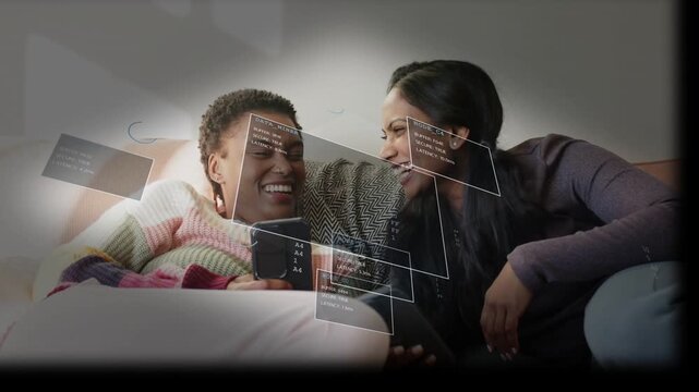 Two women on sofa sharing phones tapping screens moving floating UI panels sharing joy for tech