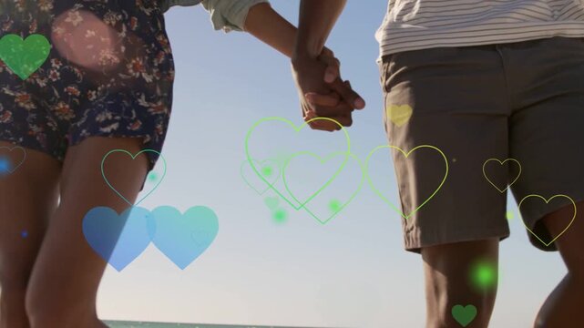 Couple walking beach to camera, camera rising, framing linked hands as hearts floating marketing