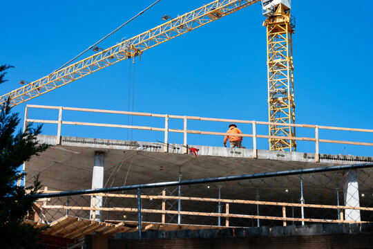 Construction worker high up on building project working on grouting structural post-tensioning wire strand holes running through concrete slab of floor
