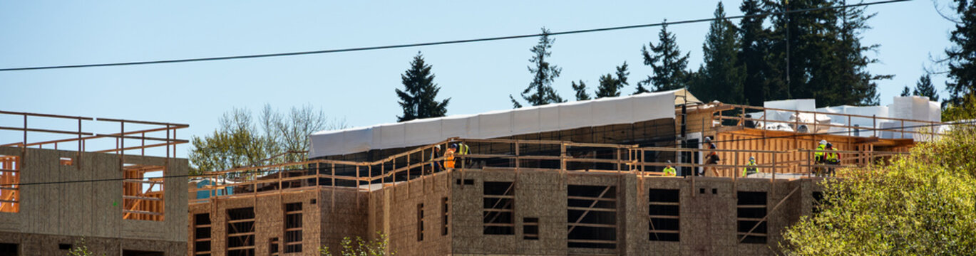 Major building commercial construction project, construction workers on top floor working on wood framing, multistory housing real estate development
