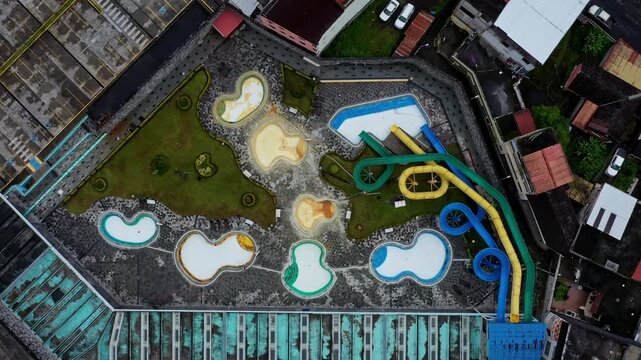 Aerial top down view of several different colored swimming pools and three large slides leading to one particular swimming pool