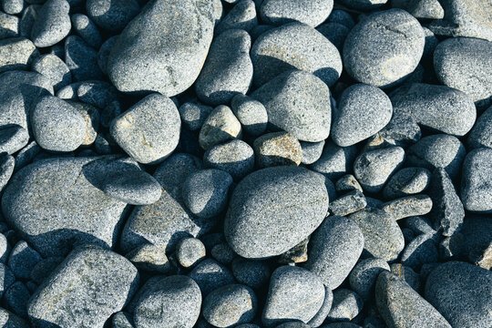 A cluster of smooth gray pebbles lies scattered along the shoreline, shaped by the constant wash of sea waves under soft sunlight.