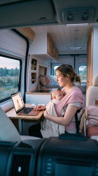 Young Mother Working Remotely on Laptop with Sleeping Baby in Carrier Inside a Camper Van