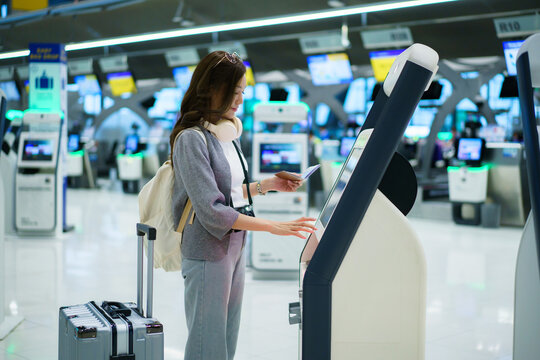 Asian woman using airport self service check in kiosk