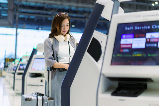 Asian woman using airport self service check in kiosk
