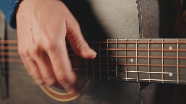 Close up hands strumming acoustic guitar, warm low light revealing finger movement across wooden body and fretboard, subtle motion blur capturing rhythmic strum, intimate songwriter practice in small