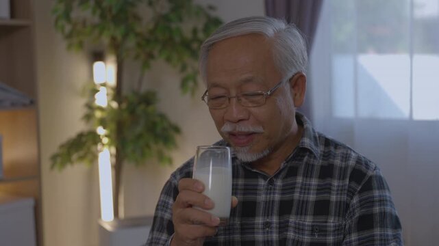 Calm senior asian man at home drinking glass of milk for bone health. An elderly gentleman enjoying peaceful lifestyle, good nutrition, and daily wellness with his beverage