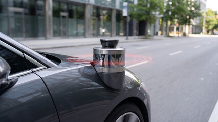 Fototapeta premium A futuristic silver device is attached to the side of a dark gray car parked on a city street with modern buildings and green trees in the background