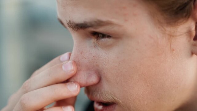 White young man rubbing nose, allergic reaction during outdoor run, freckled cheeks, light stubble, closeup profile, fingers pressing nasal bridge, seasonal pollen sensitivity, candid natural light,