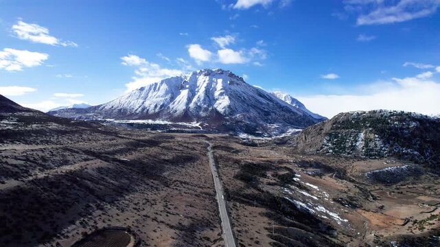 Drone view road leading to snow capped mountains in Baxoi County, Qamdo Prefecture, Tibet, China, high angle view of cars driving on asphalt road on Qinghai-Tibet Plateau, 4k real time travel footage.