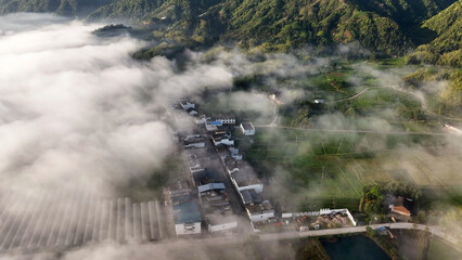 Fototapeta premium Aerial view of a rural village nestled among misty mountains and terraced farmland at dawn