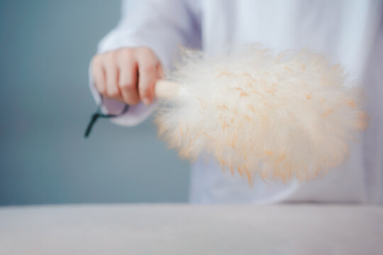 Close up of a person using a soft feather duster to clean dust from furniture surface, showcasing gentle household cleaning routine, hygiene, maintenance, and minimal lifestyle.