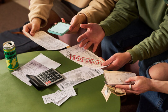 Close up of students reviewing overdue bills, counting cash, checking smartphone, using calculator. Suitable for budgeting, student debt, personal finance, payment stress campaigns