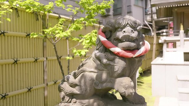 Stone guardian dog Komainu with red bib at Japanese shrine.