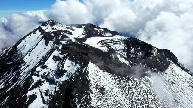 Aerial view, turning around the summit of the active Tungurahua volcano in the Andes of Ecuador, showing an in snow covered mountain with a larger crater