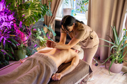 Professional masseuse making special relaxing back massage for woman client using hands, female on spa bed receiving massage treatment, beauty procedures and regular body care for healthy living.