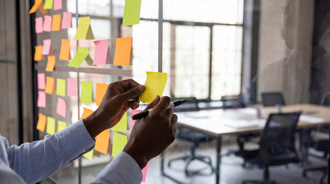 African American person's hands writing on a yellow sticky note.