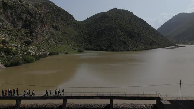 Drone aerial shot of Oyoun El Samak dam in Akkar Lebanon showing calm water, surrounding mountains and people walking on the bridge