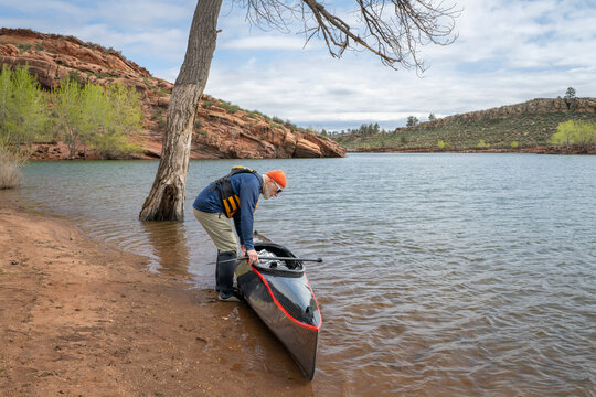 senior paddler is launching his decked touring canoe on shore of Horsetooth Reservoir - early spring scenery of Colorado foothills