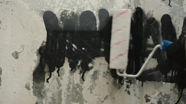 Closeup paint roller covering graffiti on weathered concrete wall, gloved hand applying thick black coat to conceal tags, heavy drips and streaks, tactile surface texture, focused maintenance action