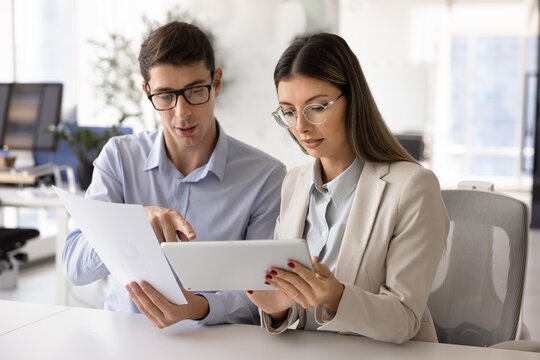 Team members collaborating on project details, discussing marketing plan, analyzing financial data, reviewing proposal using digital tablet and printed documents at modern workplace. Analytics, tech