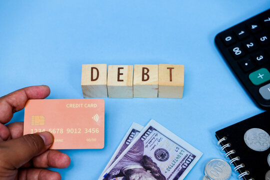 Debt concept: hand holding credit card, money, coins, calculator on blue background