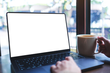 Fototapeta premium Mockup image of a woman working on laptop computer with blank white desktop screen while drinking coffee in cafe