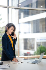 Obraz premium Businesswoman talking on smart phone and taking notes working in corporate office.