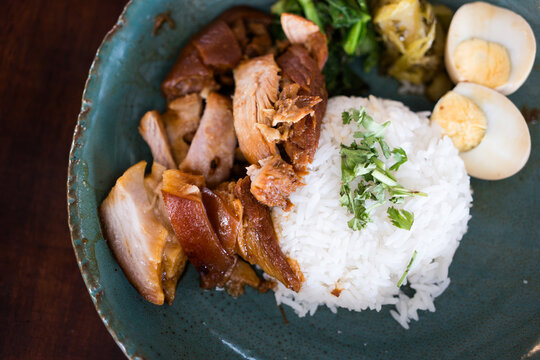 Stewed leg pork with sweet gravy sauce served with boiled vegetable and boiled egg on green ceramic dish