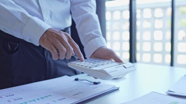 Businessman holding and press botton on calculator over documents